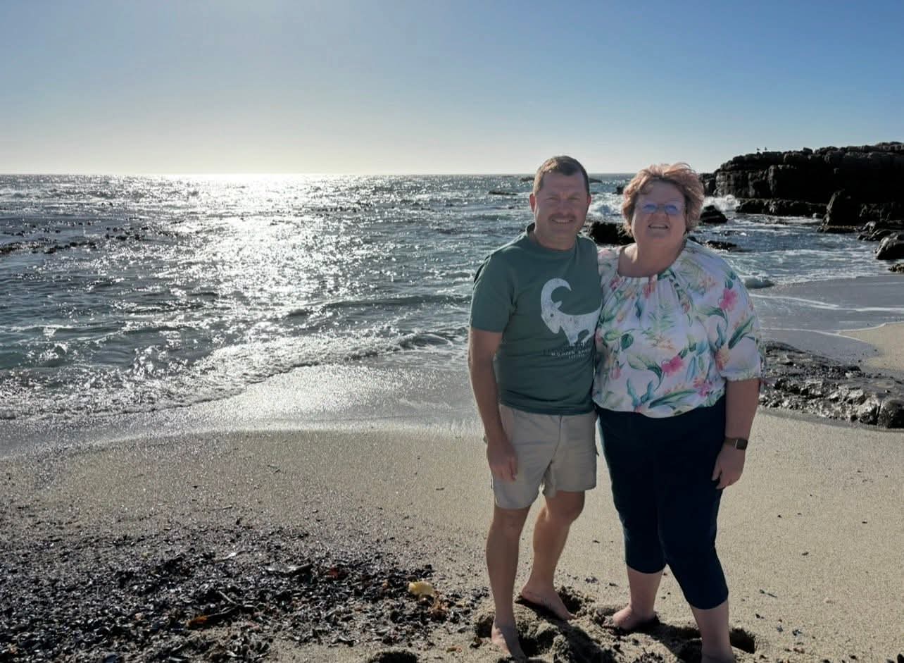 Angelo and his mum standing together on a sunlit beach
