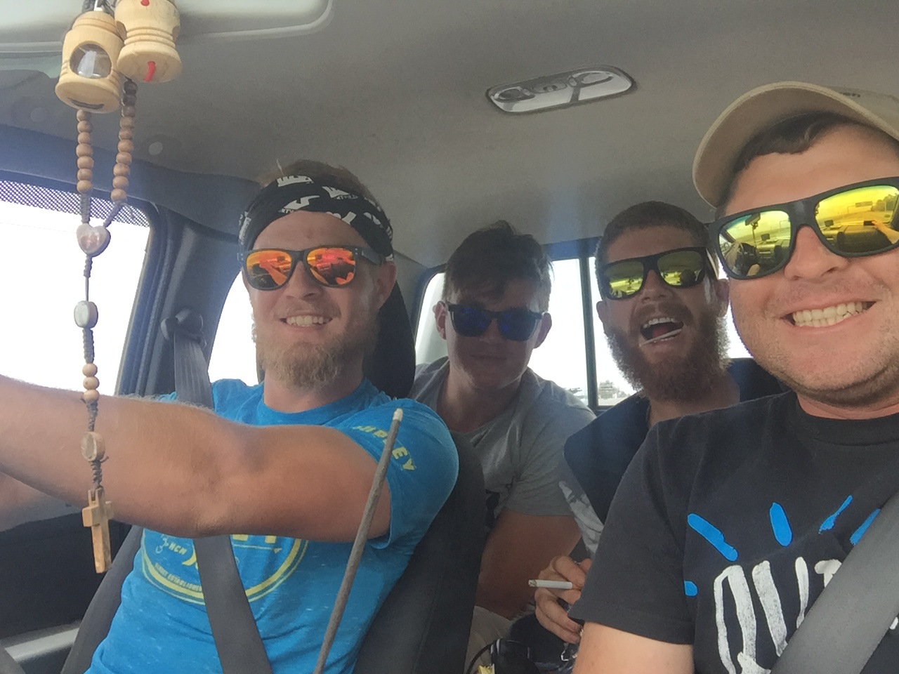 Four friends in sunglasses smiling inside a bakkie on a road trip