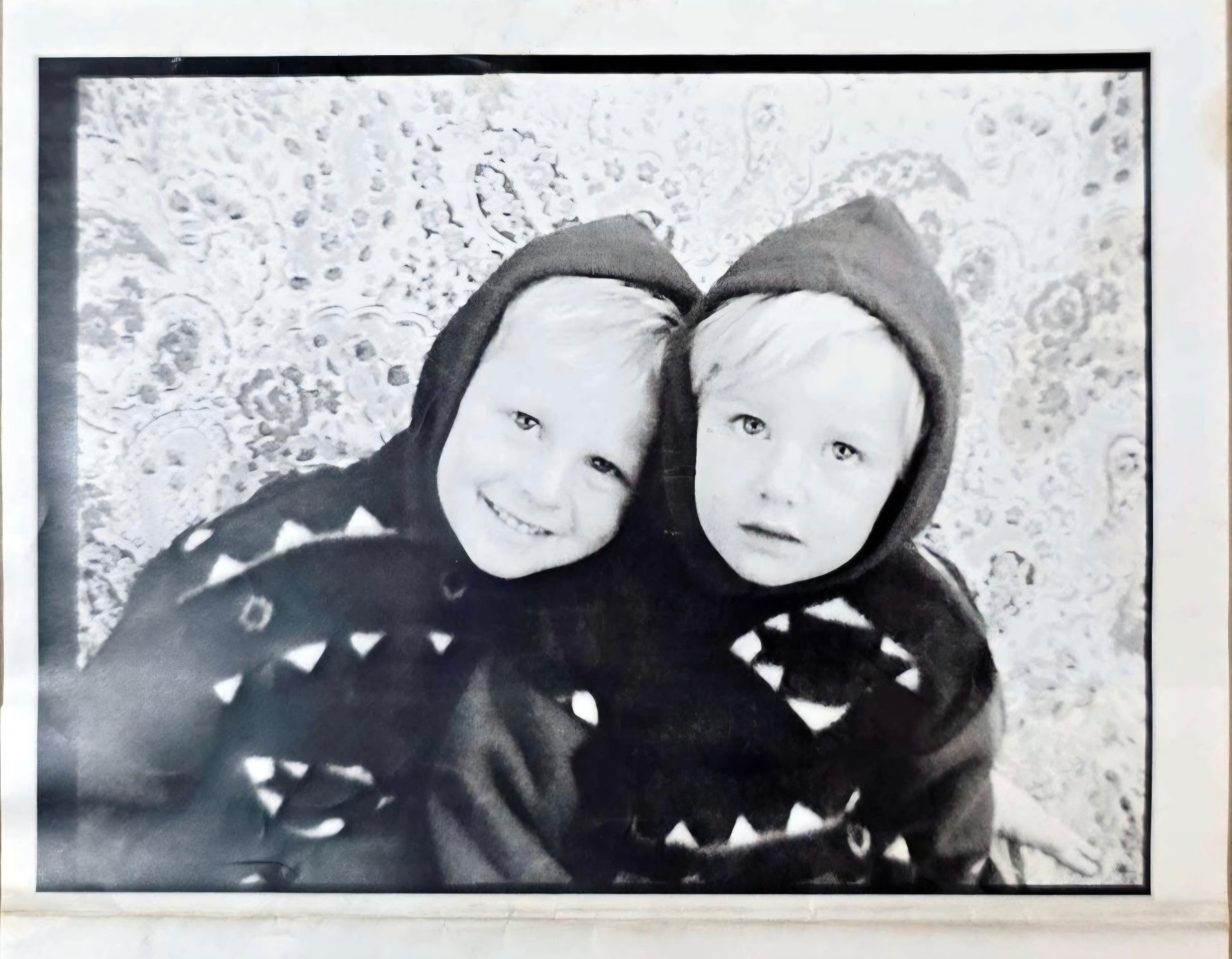 A black and white childhood photo of Angelo and his sister in matching hooded jackets