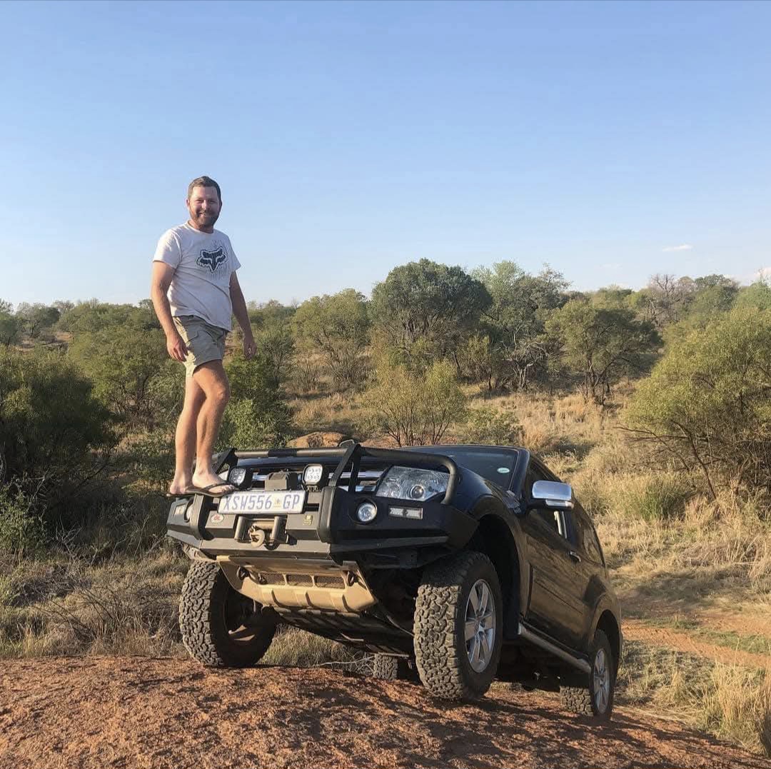 Angelo standing on the bull bar of a 4x4 SUV on a dirt mound in the bushveld
