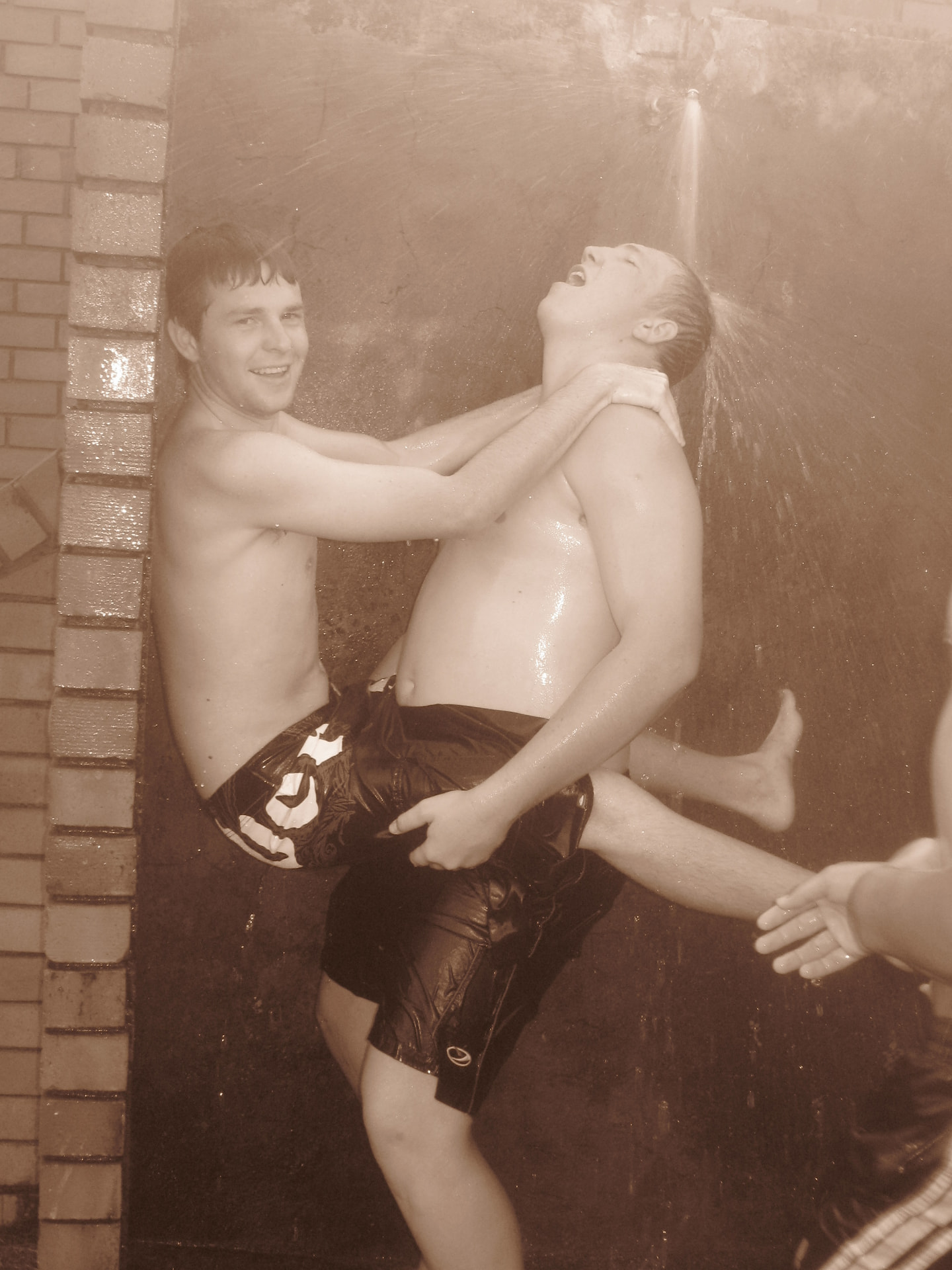 A sepia photograph of Angelo and friends laughing under an outdoor shower at church camp