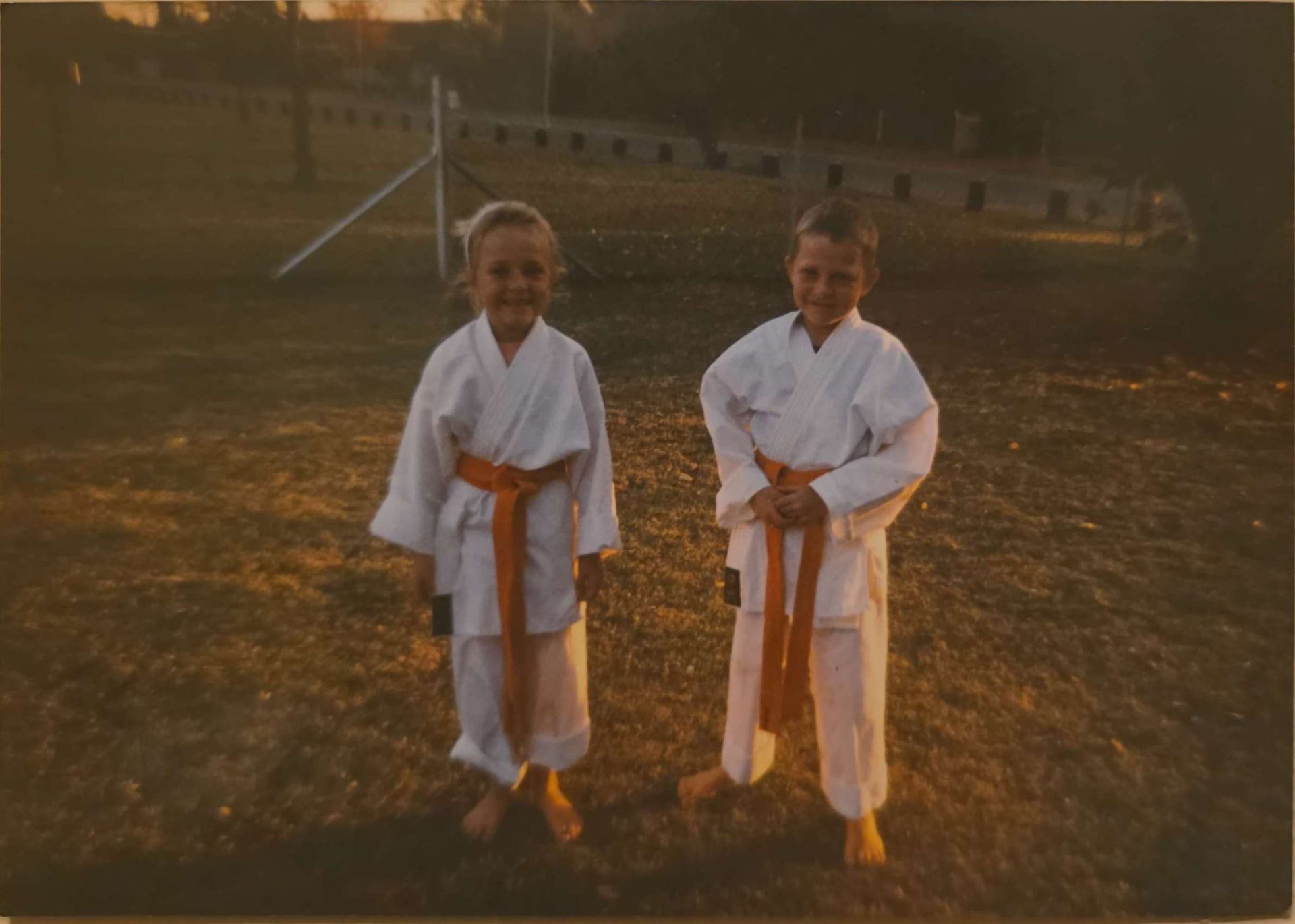 Angelo and his sister in white karate uniforms with orange belts on a field
