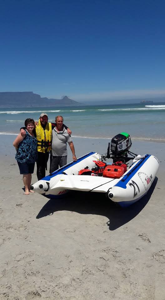 Three people standing together beside an inflatable boat on the beach