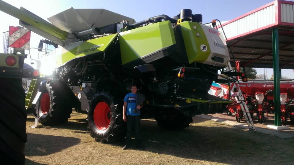 Angelo standing beside a large green combine harvester at an exhibition