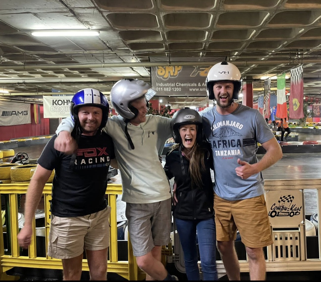 Four friends in helmets celebrating at an indoor go-kart track