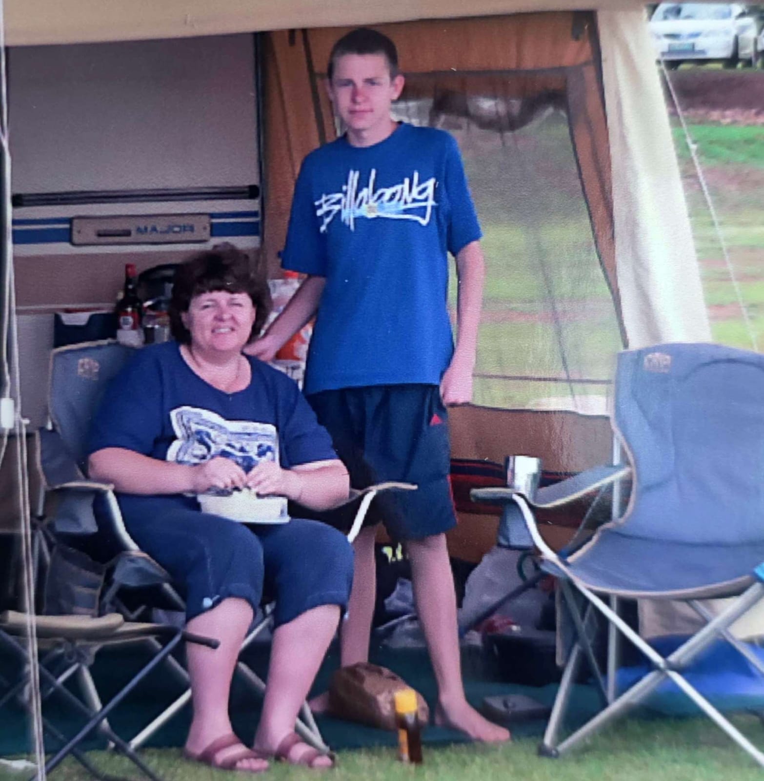 Teenage Angelo standing beside his mum at a camping site