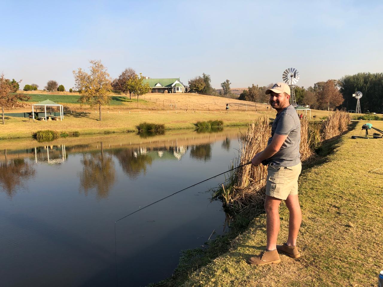 Angelo smiling with his fishing rod on the bank of a farm dam at golden hour