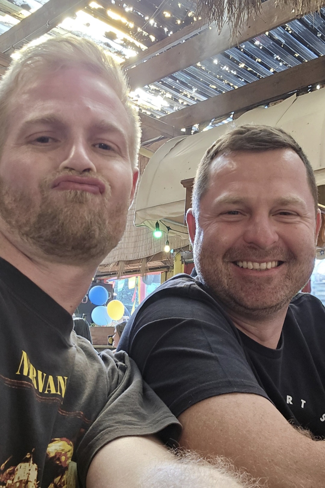 Angelo and a friend smiling in a selfie at an outdoor bar
