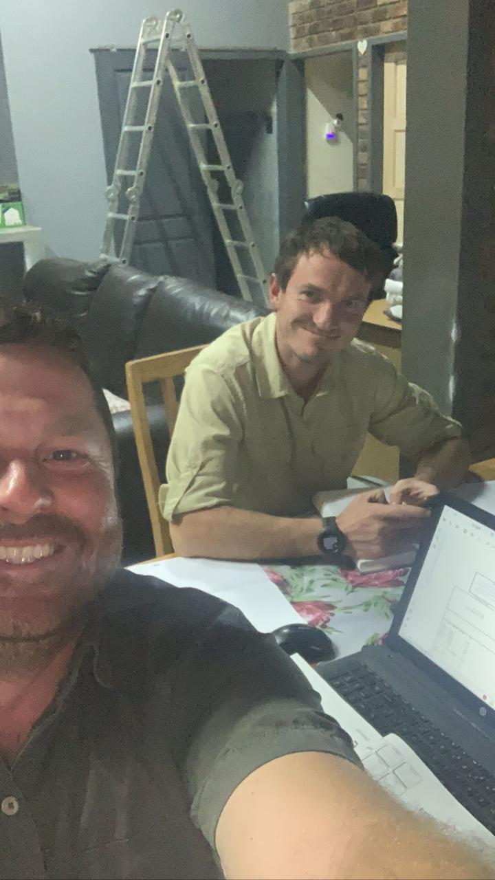 Angelo taking a selfie beside a friend working at a table with a laptop