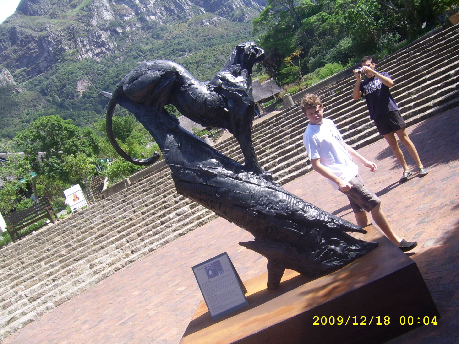 Angelo standing beside a large black leopard sculpture with a mountain rising behind