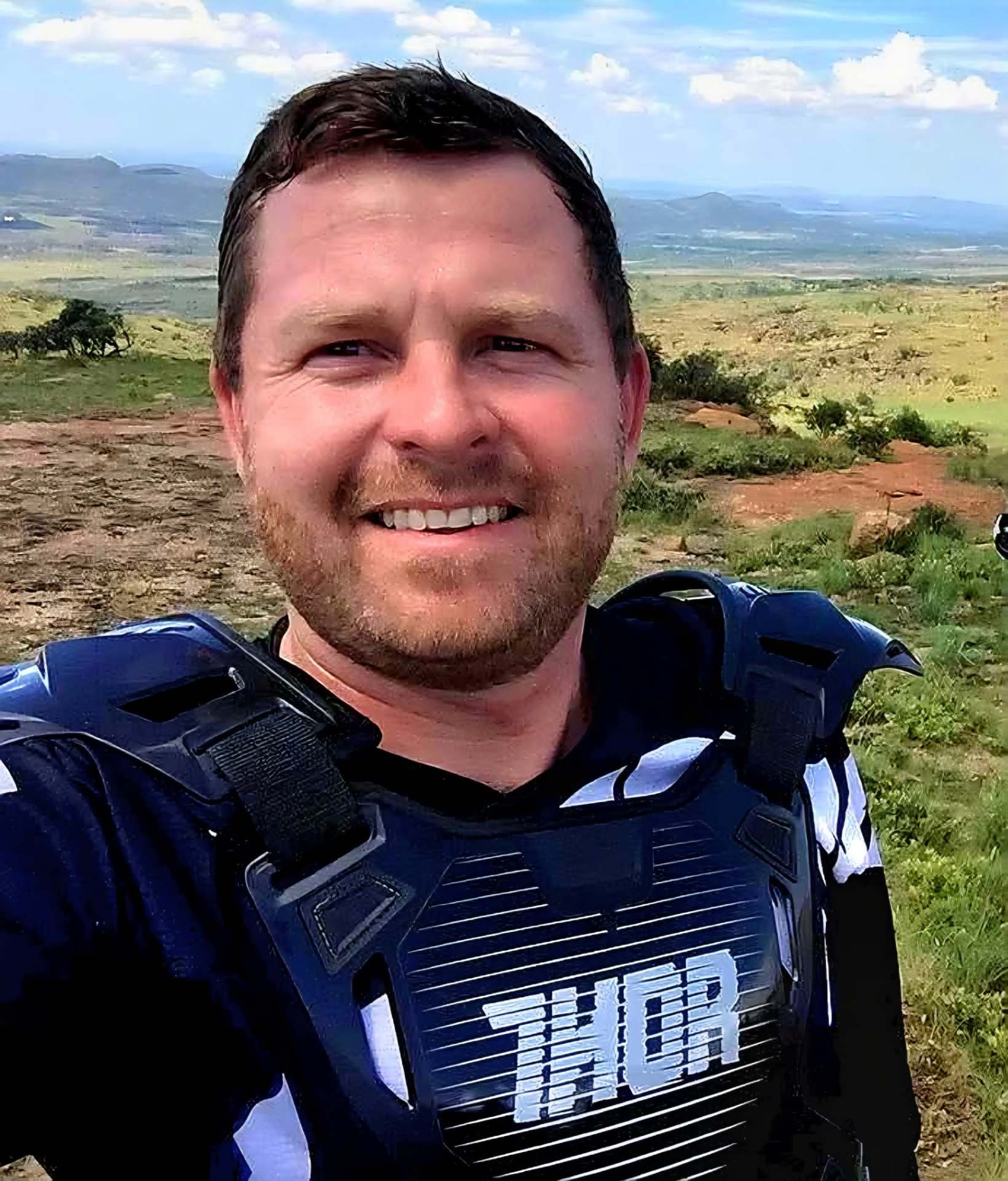 Angelo smiling in riding gear against a sweeping hillside view