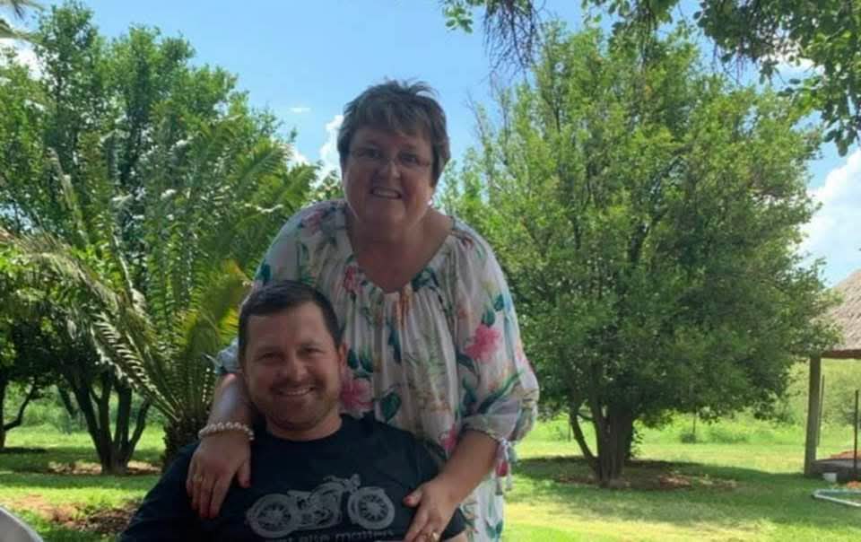 Angelo's mum resting her hands on his shoulders in a sunlit garden
