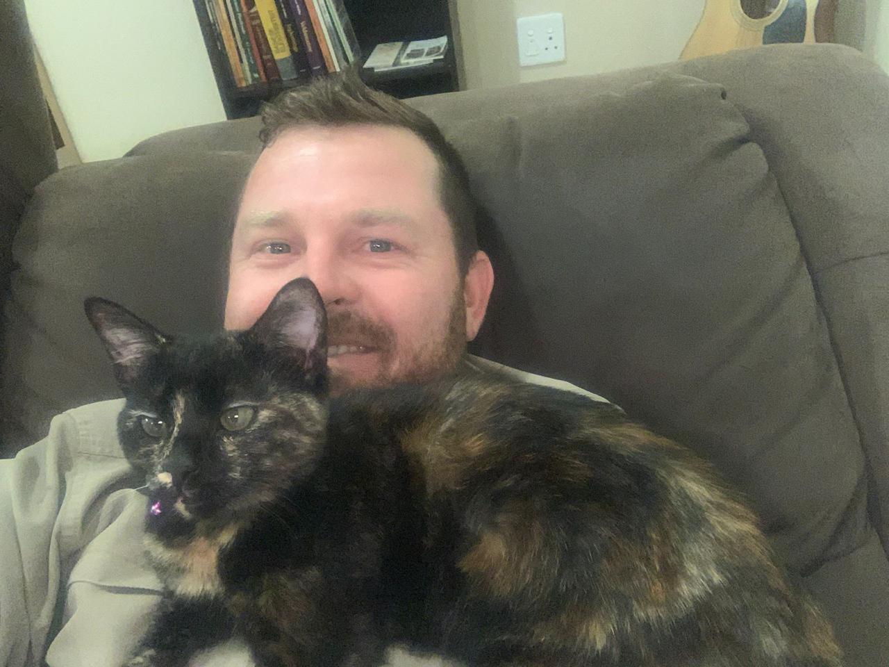 Angelo taking a cozy selfie on the couch with his tortoiseshell cat