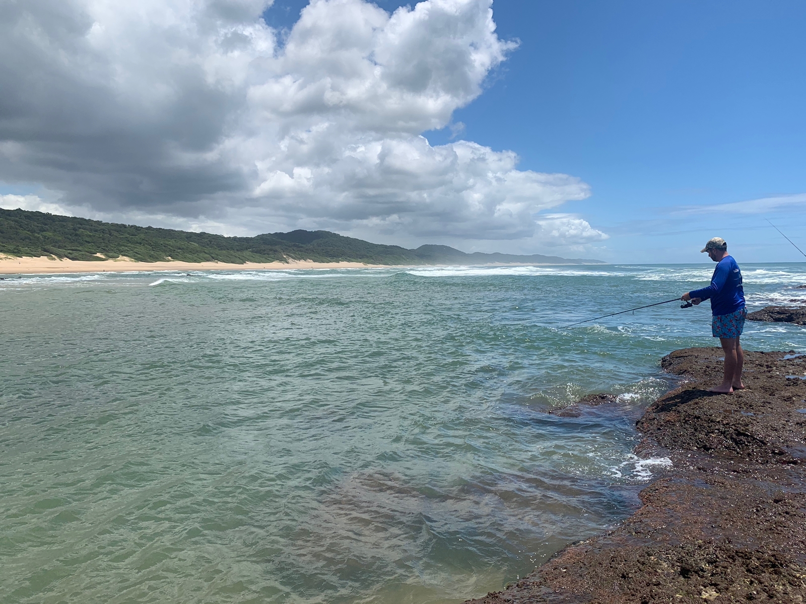 Angelo fishing from the rocks on a wild green coastline beneath big summer clouds