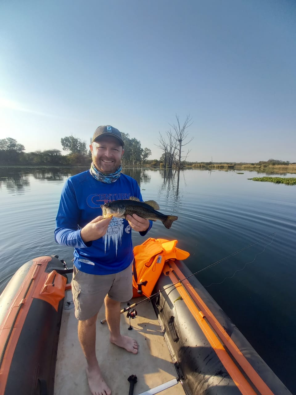 Angelo holding a fish on an inflatable boat on a calm river