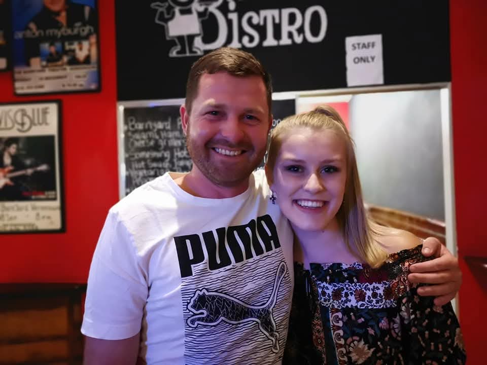 Angelo and a friend smiling together in front of a bistro sign