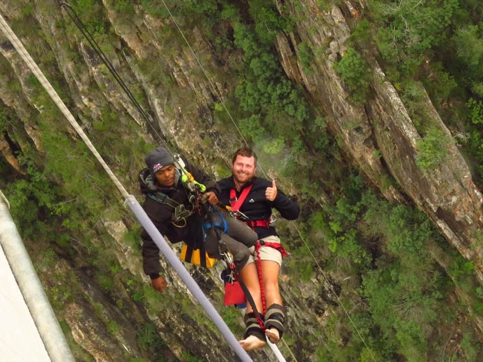 Angelo and a companion suspended on ropes above a rocky gorge