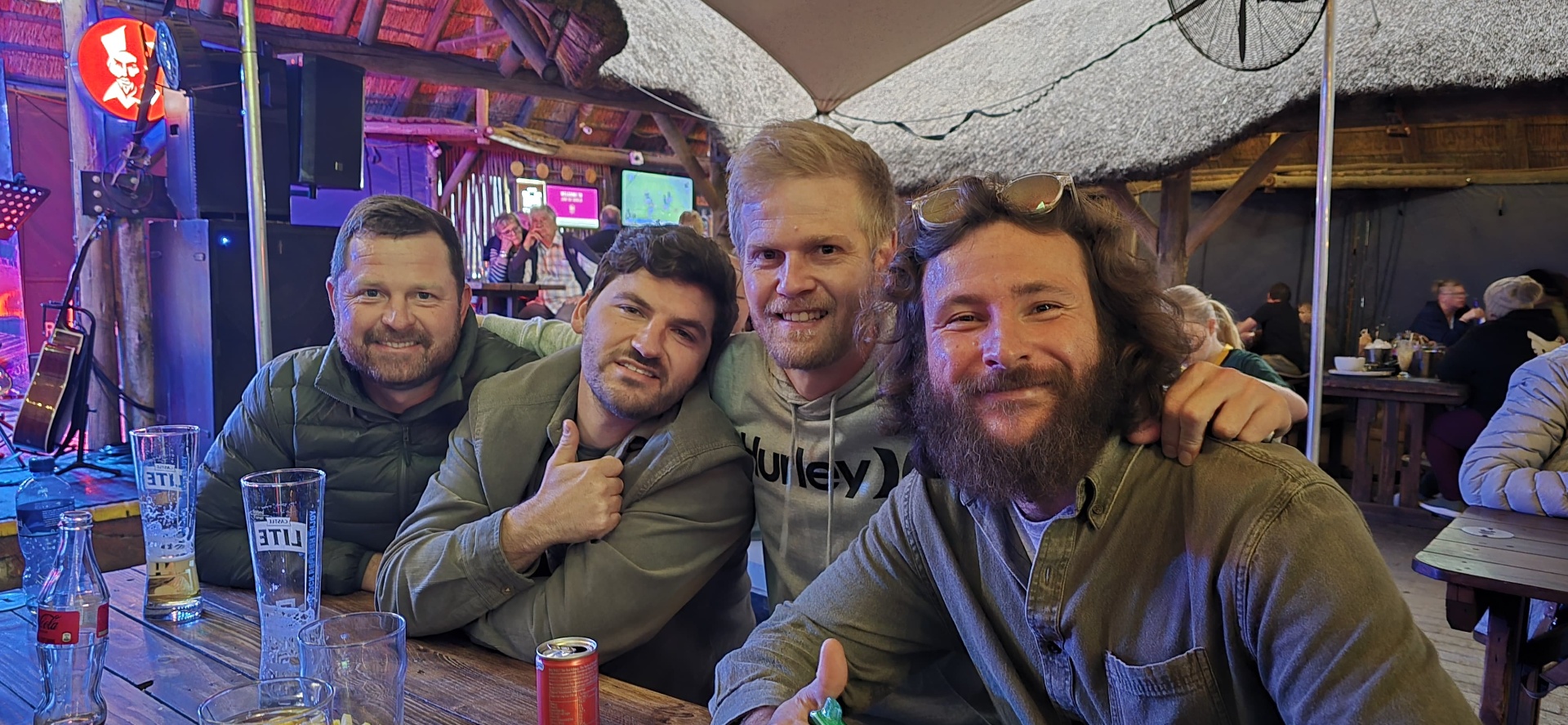 Four friends together at a table under a thatched roof