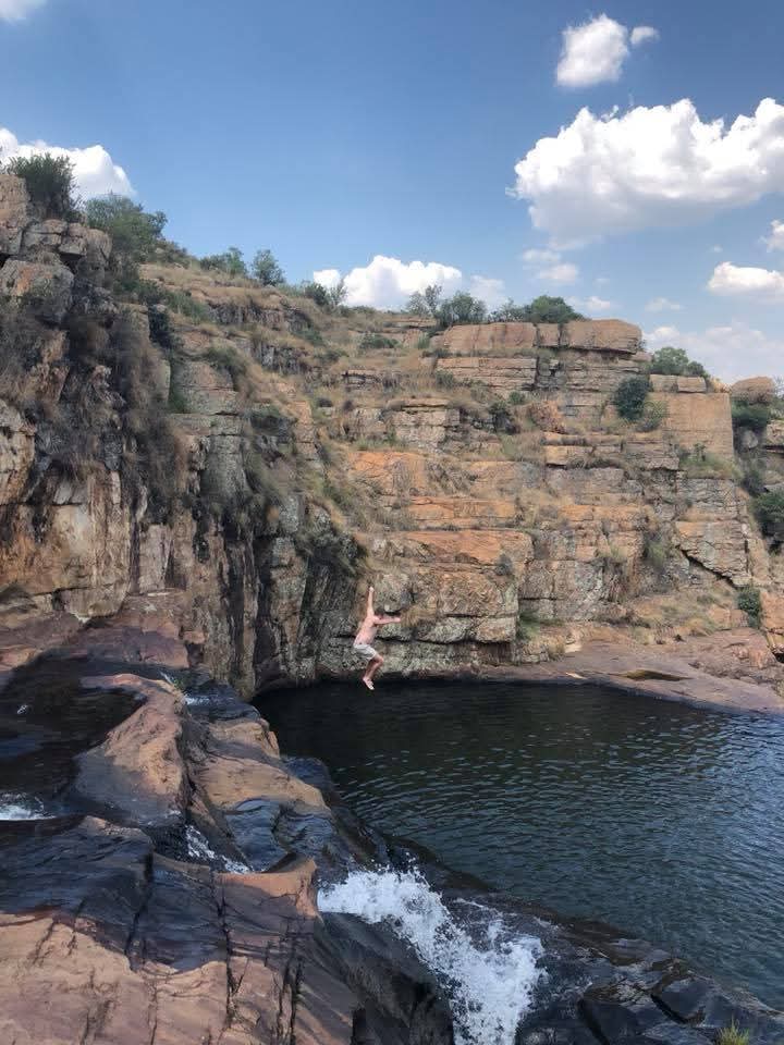 Angelo jumping toward a natural pool surrounded by layered rock cliffs