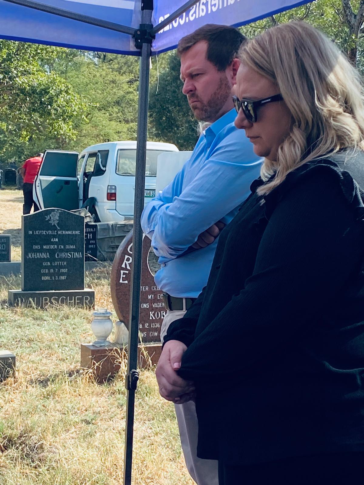 Angelo and a family member standing solemnly beside a gravesite