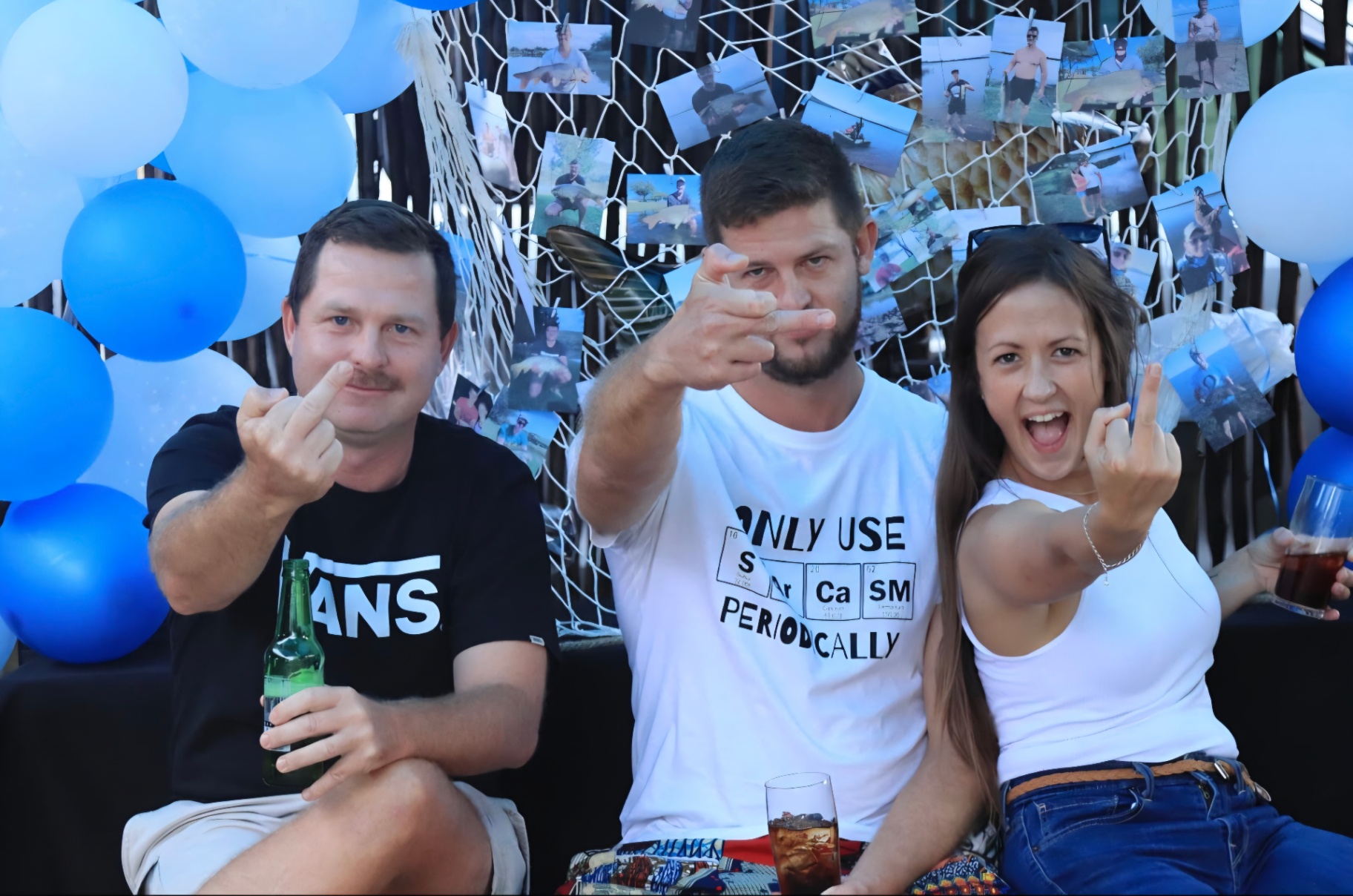 Three friends pulling faces at a fishing-themed party with blue balloons
