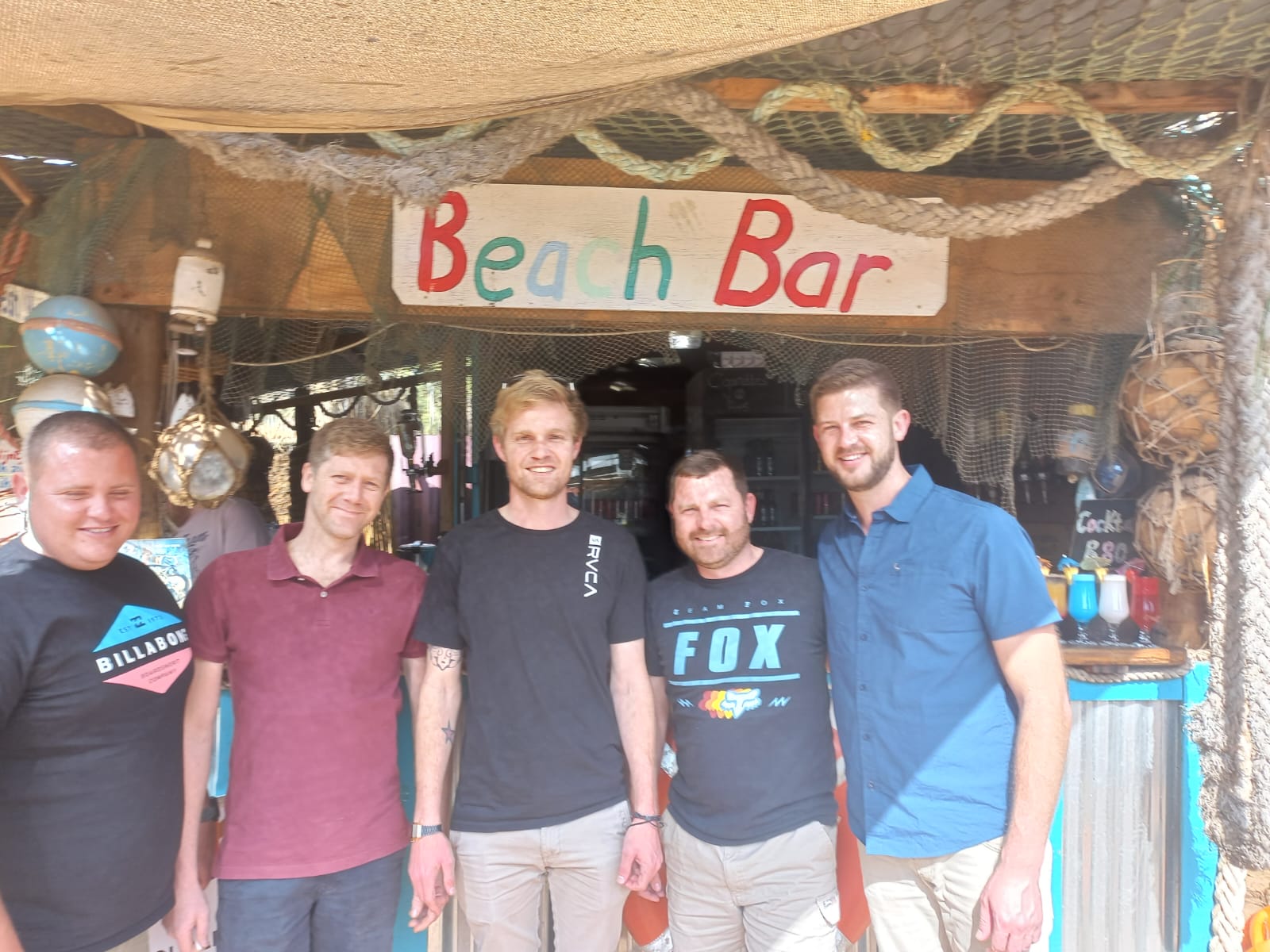Five friends standing together in front of a beach bar sign