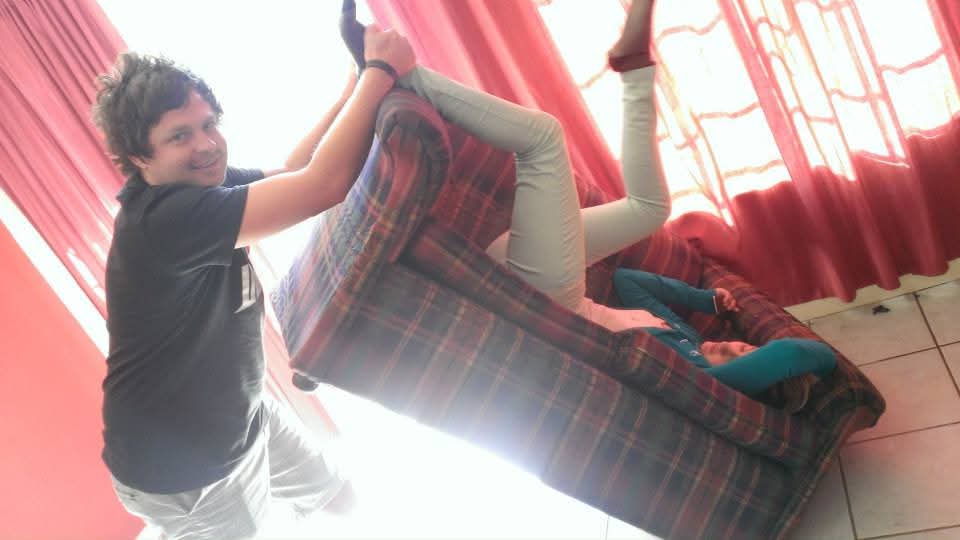 Friends sharing a playful moment around an armchair beside red curtains