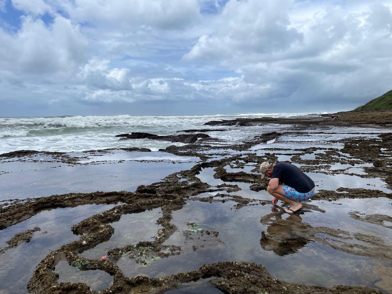 Angelo crouching over the tidal rock pools along a stormy coastline