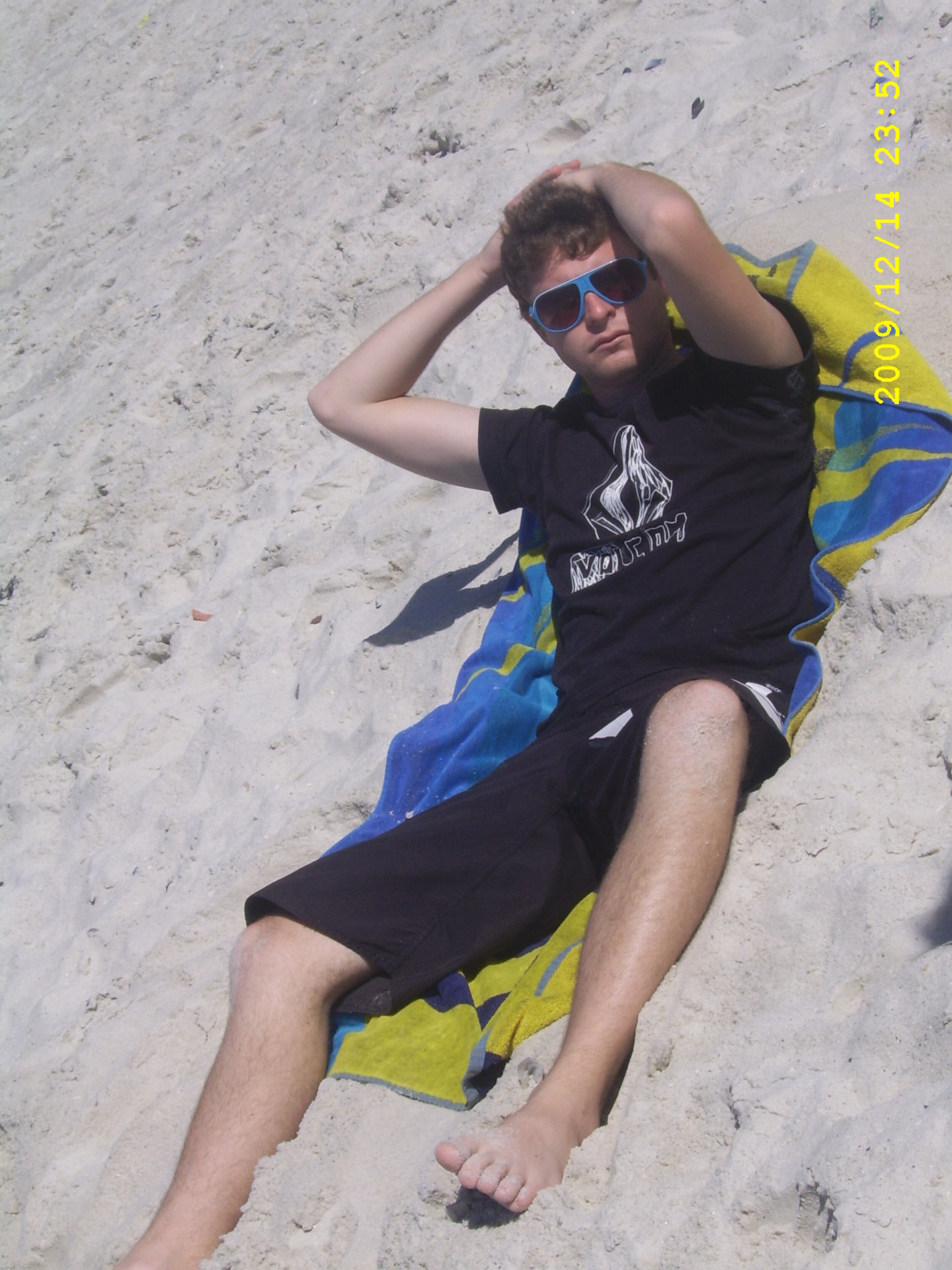 A young Angelo relaxing on a beach towel in blue sunglasses