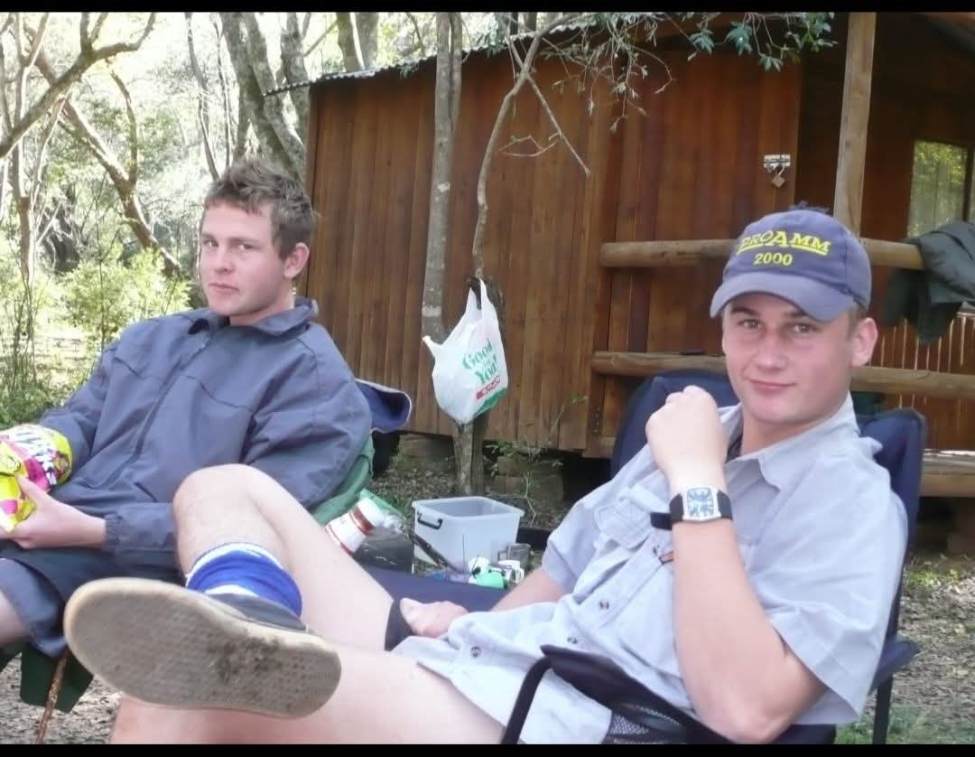 Two friends relaxing in camp chairs outside a wooden cabin in the forest