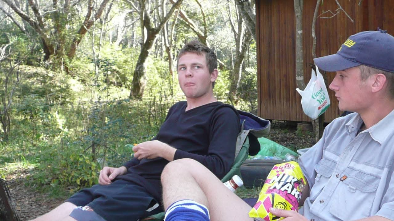 Angelo and a friend relaxing with snacks outside a wooden cabin