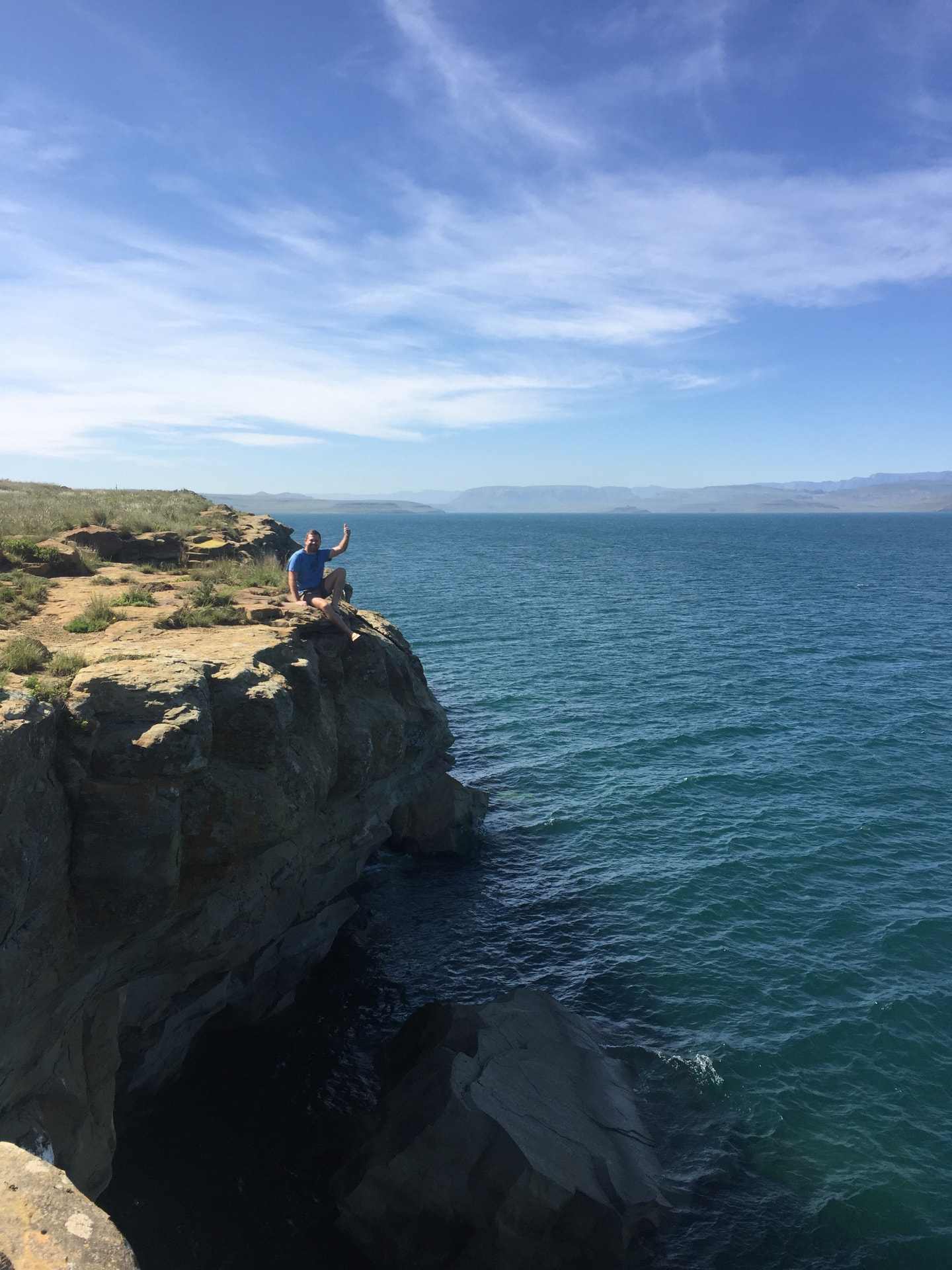 Angelo waving from a rocky cliff above the blue lake