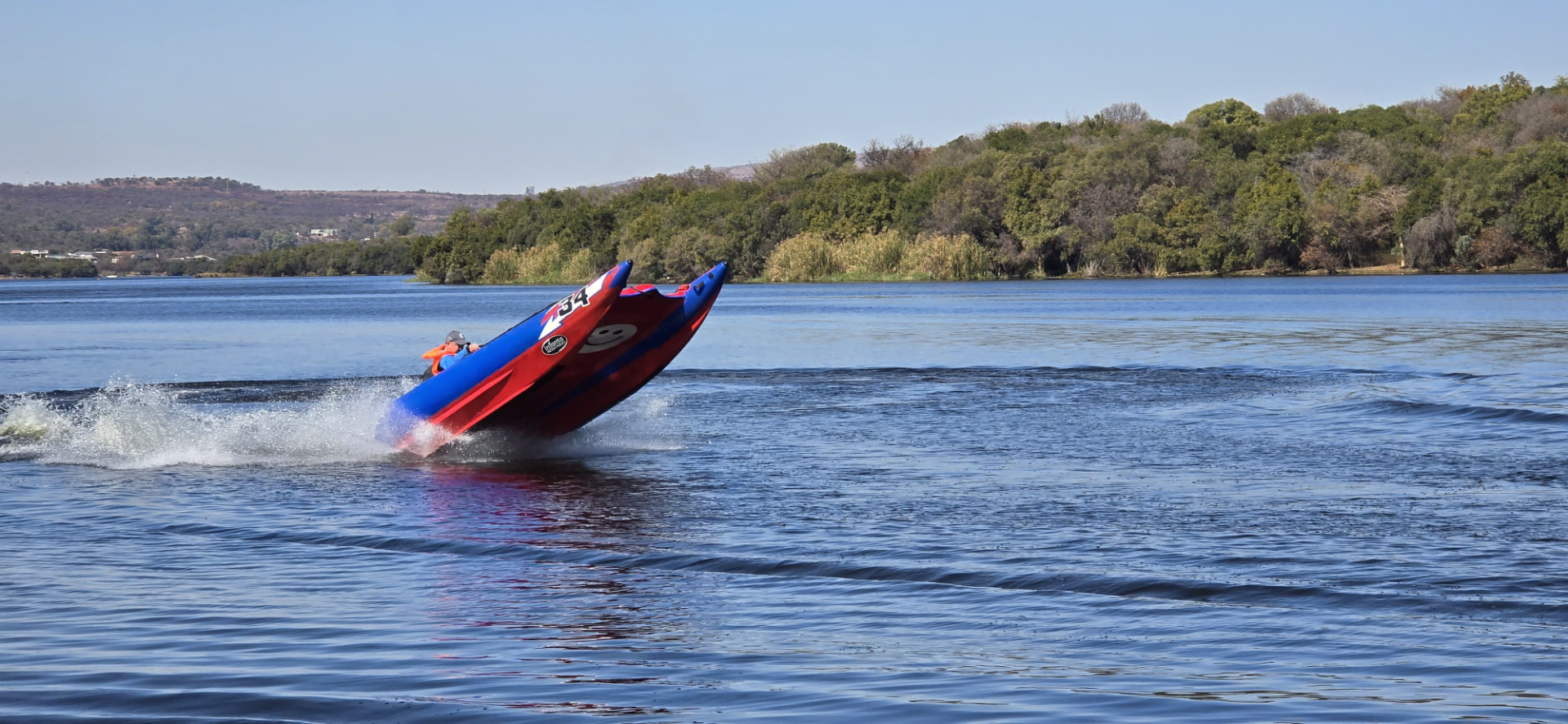 A wide view of the number 34 boat lifting over the water against wooded hills