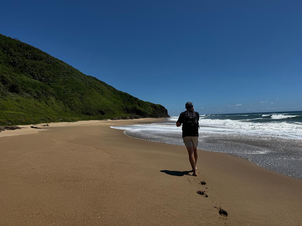 Angelo walking alone along a wild beach, his footprints trailing behind him