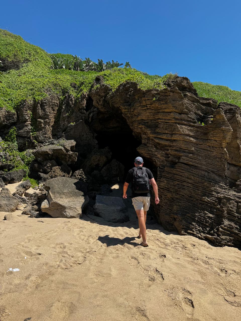 Angelo with his backpack walking into the dark mouth of a coastal sea cave