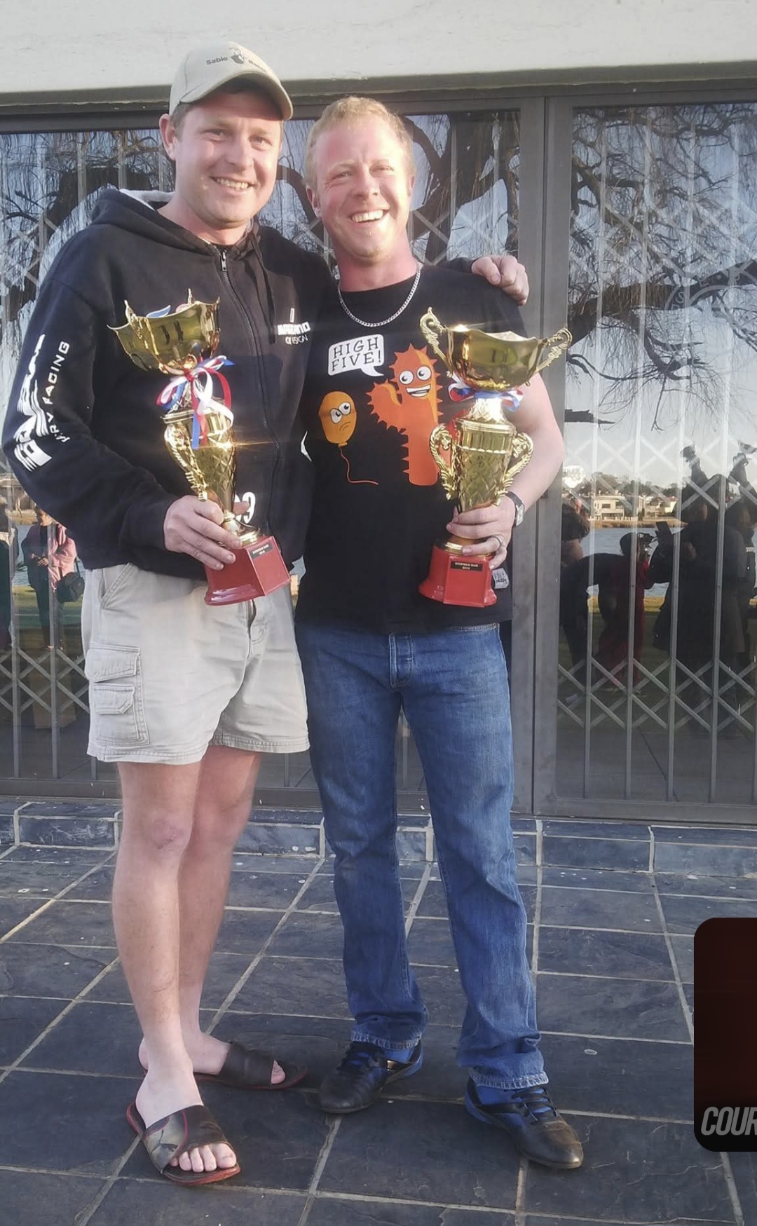 Two friends standing with trophies outside a building