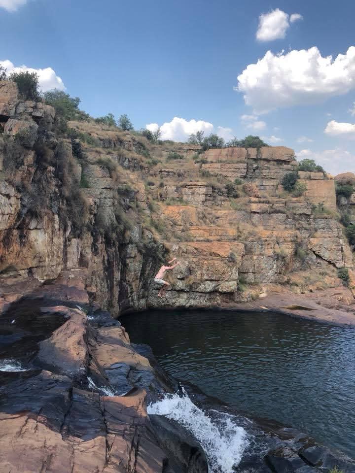 Angelo descending toward the water during a jump into a rocky natural pool