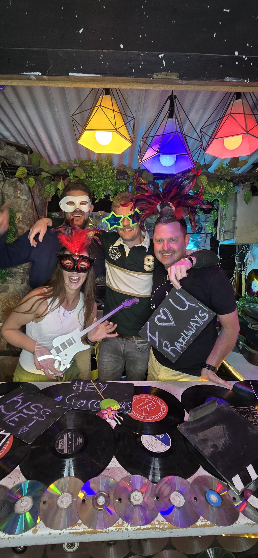 Friends in masks and costumes laughing behind a record-covered bar
