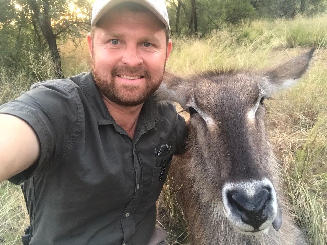 Angelo taking a close selfie beside a waterbuck at golden hour