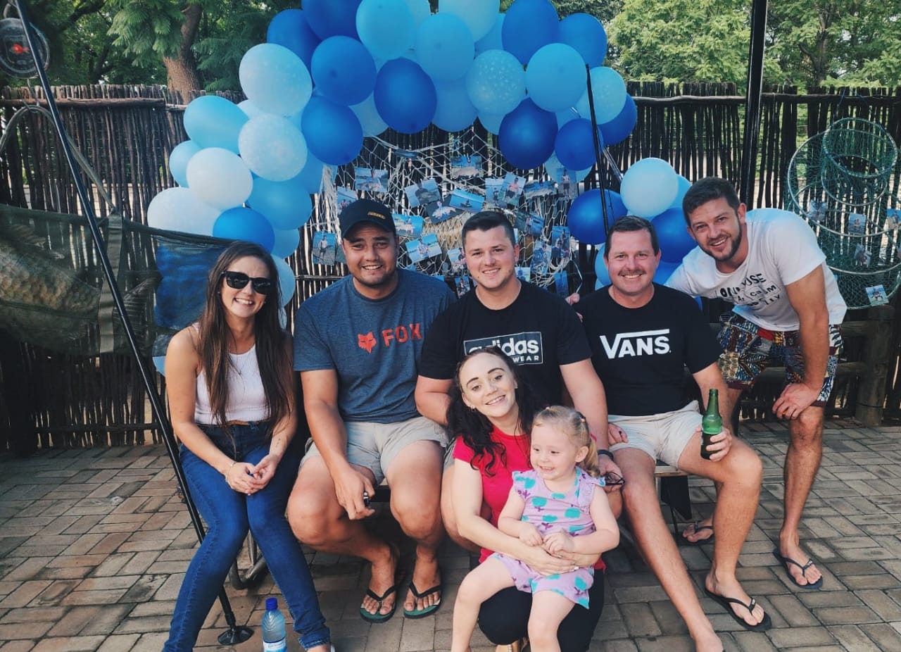 Friends seated under a blue balloon arch with a little girl in front
