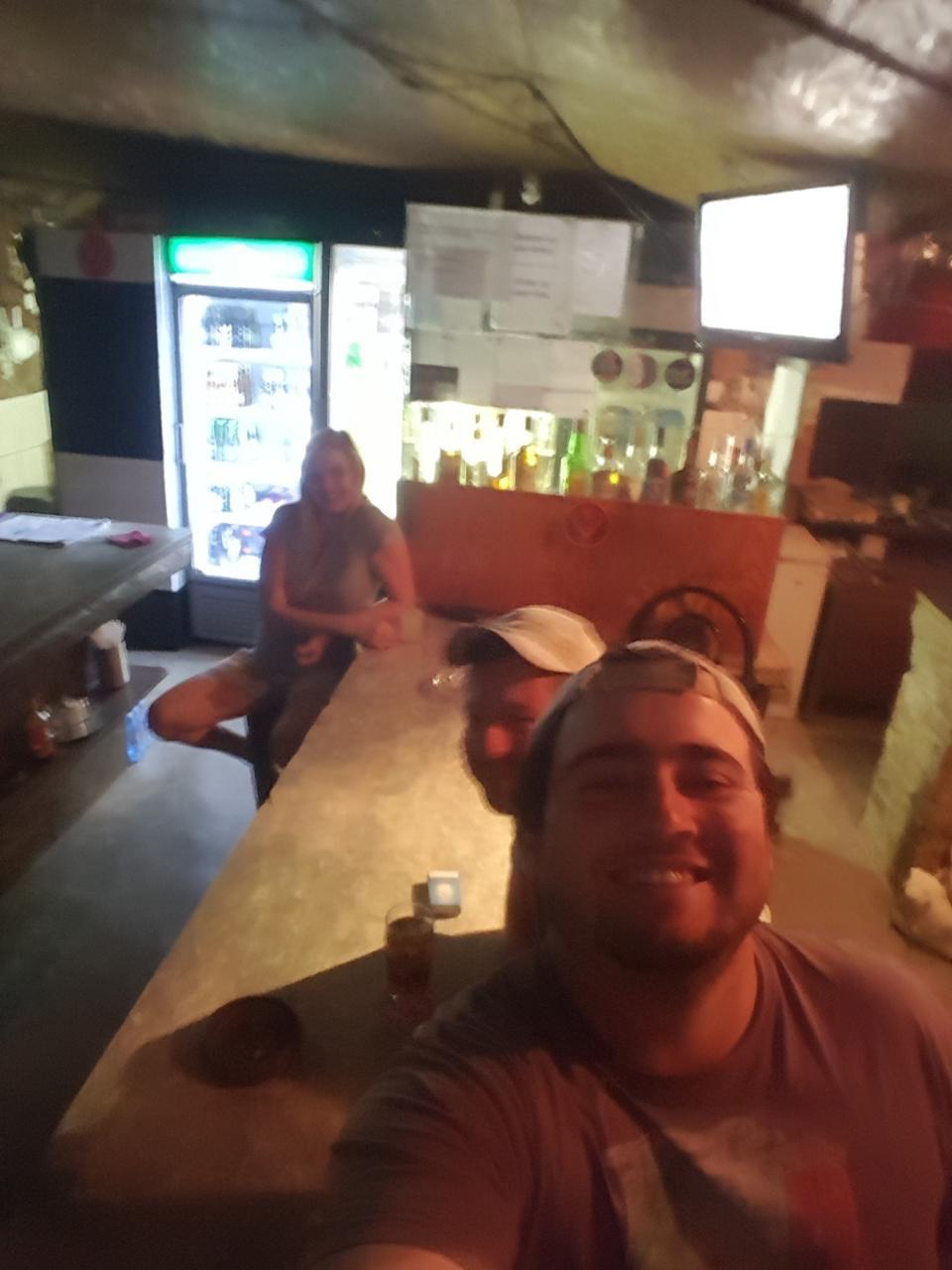 Angelo taking a selfie with friends at a dimly lit bush bar