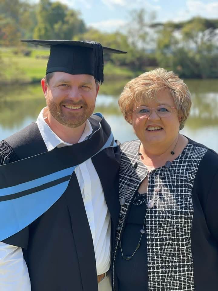 Angelo in graduation regalia posing with a family member outdoors