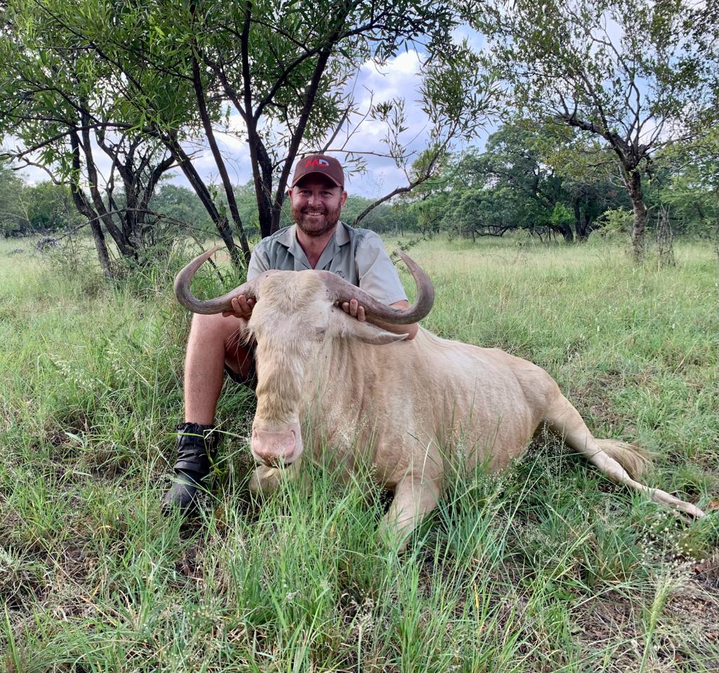 Angelo kneeling beside a golden wildebeest in green summer grass