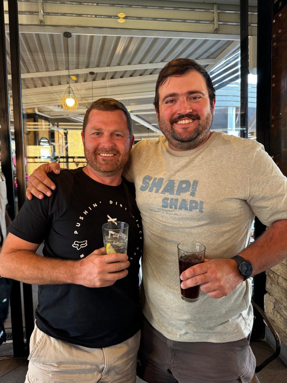 Angelo and a friend with their arms around each other over drinks at a restaurant