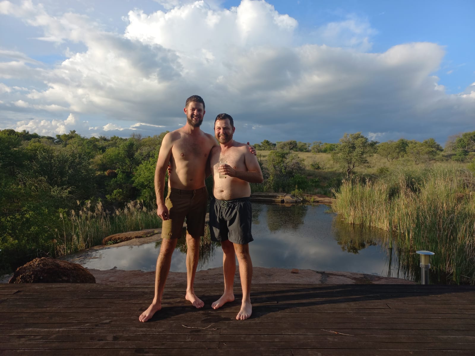 Angelo and his best friend standing together on a deck beside a rock pool in the bushveld
