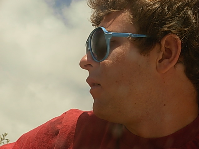A young Angelo wearing blue sunglasses and a red shirt outdoors