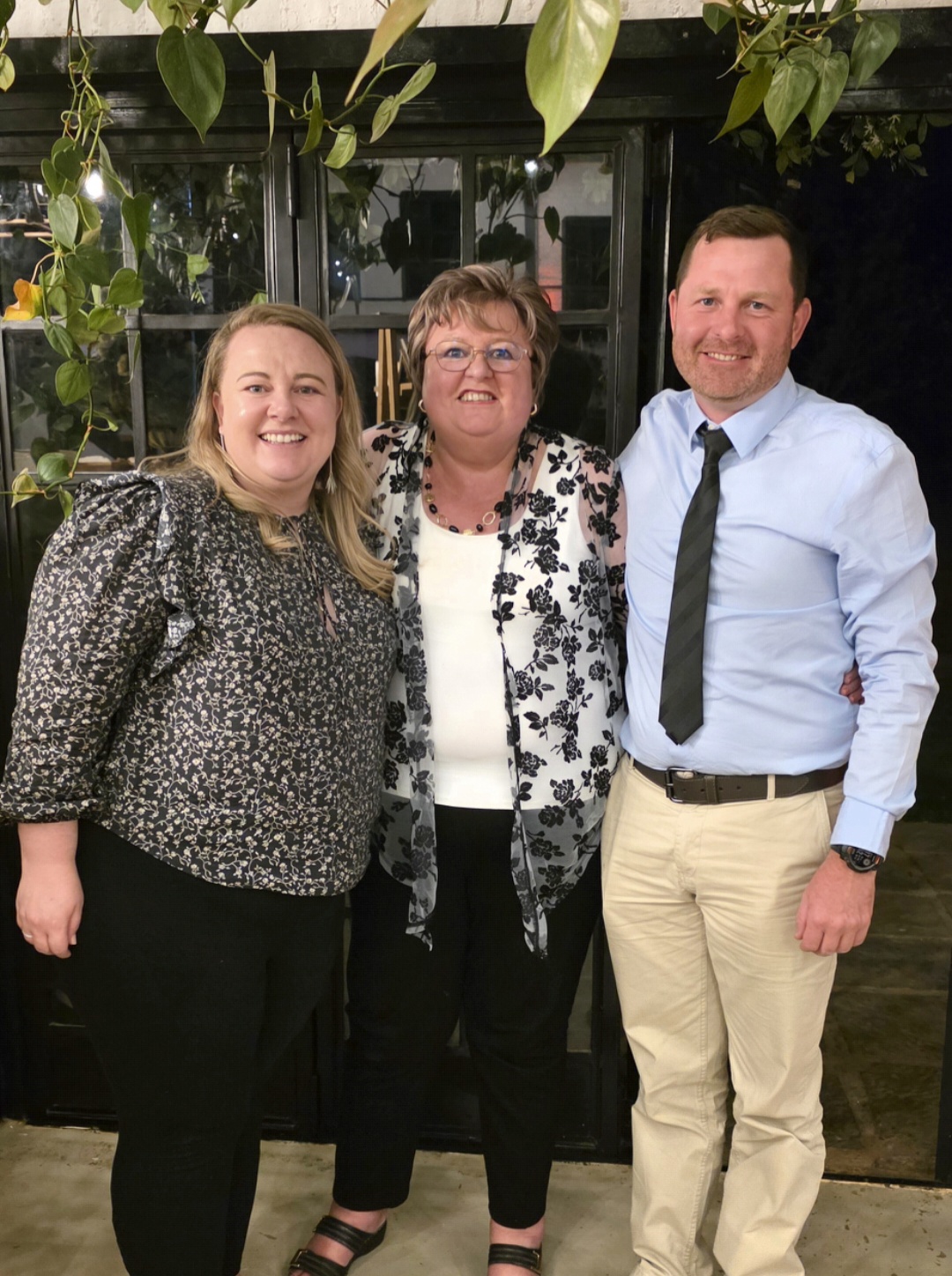 Angelo with two family members indoors beneath hanging plants