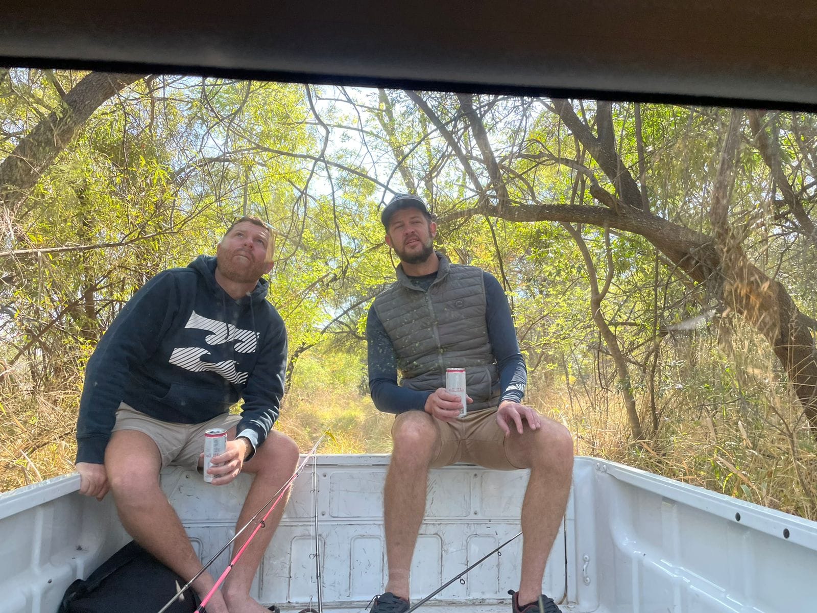 Angelo and his best friend with fishing rods on the back of a bakkie under the trees