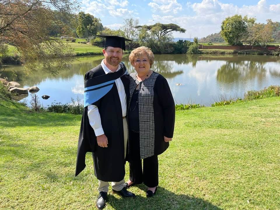 Angelo in full graduation gown with a family member beside a pond