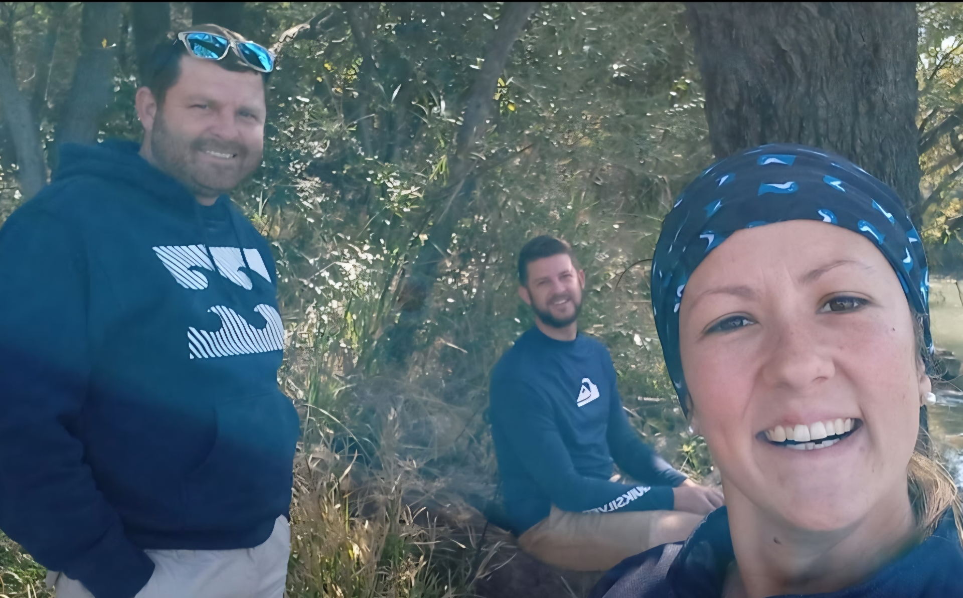 Angelo and two friends smiling together on a shady riverbank